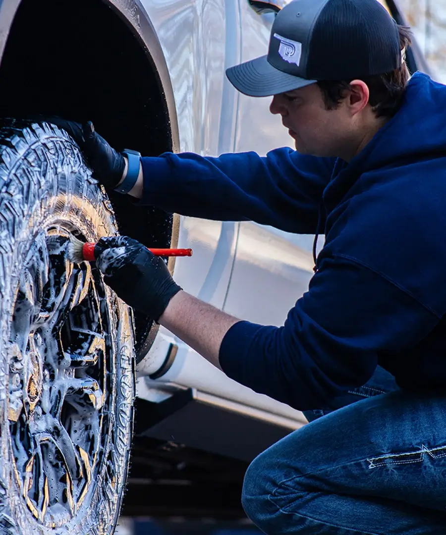 A man scrubbing a soapy truck tire with a small red brush. 