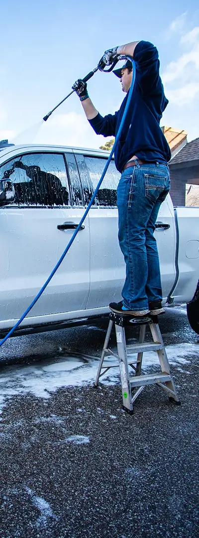 A man standing on a small latter and spraying the top of a truck during vehicle detailing near me